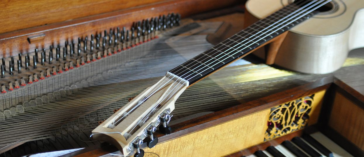 Gitarre liegt auf einem offenen Klavierflügel. 