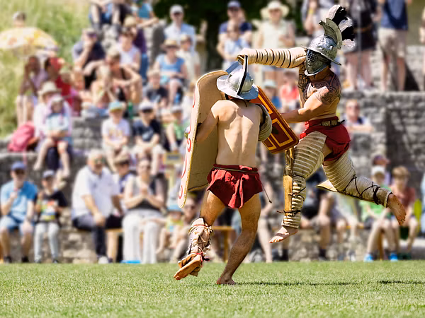 Zwei römische Gladiatoren kämpfen im Amphitheater Vindonissa gegeneinander. Im Hintergrund in Unschärfe viel Publikum.