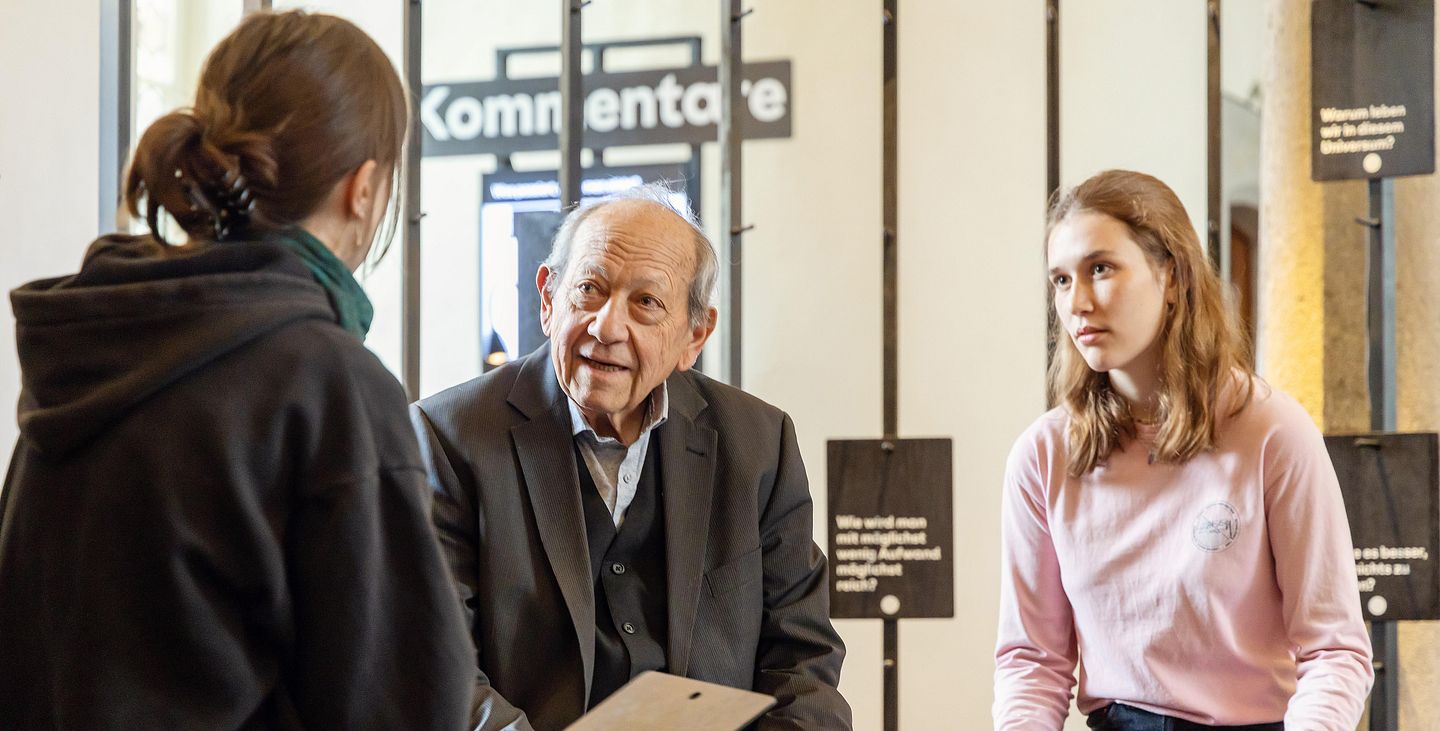 Ein älterer Mann im Gespräch mit zwei jugendlichen Frauen.