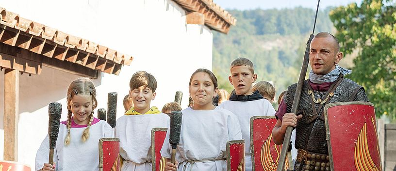 Ein römischer Legionär marschiert mit Mädchen und Buben nebeneinander im Legionärspfad Vindonissa.