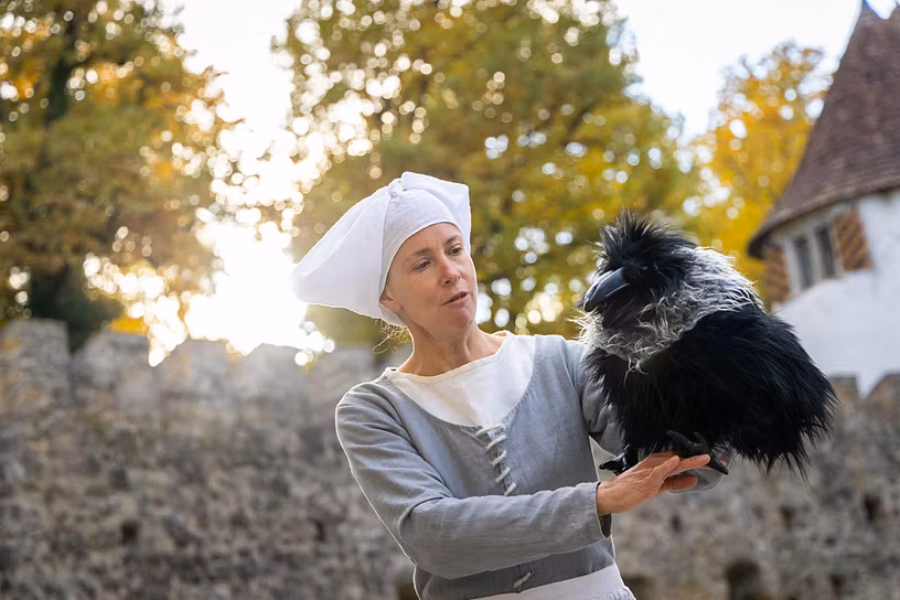 Eine mittelalterlich gekleidete Frau auf Schloss Hallwyl. Sie hält ein Vogelpuppe (Dohle) in der Hand.