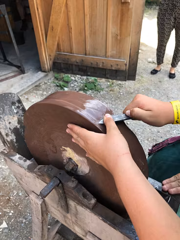 Detailaufnahme von zwei Händen, die an einem Stein ein Messer schleifen.