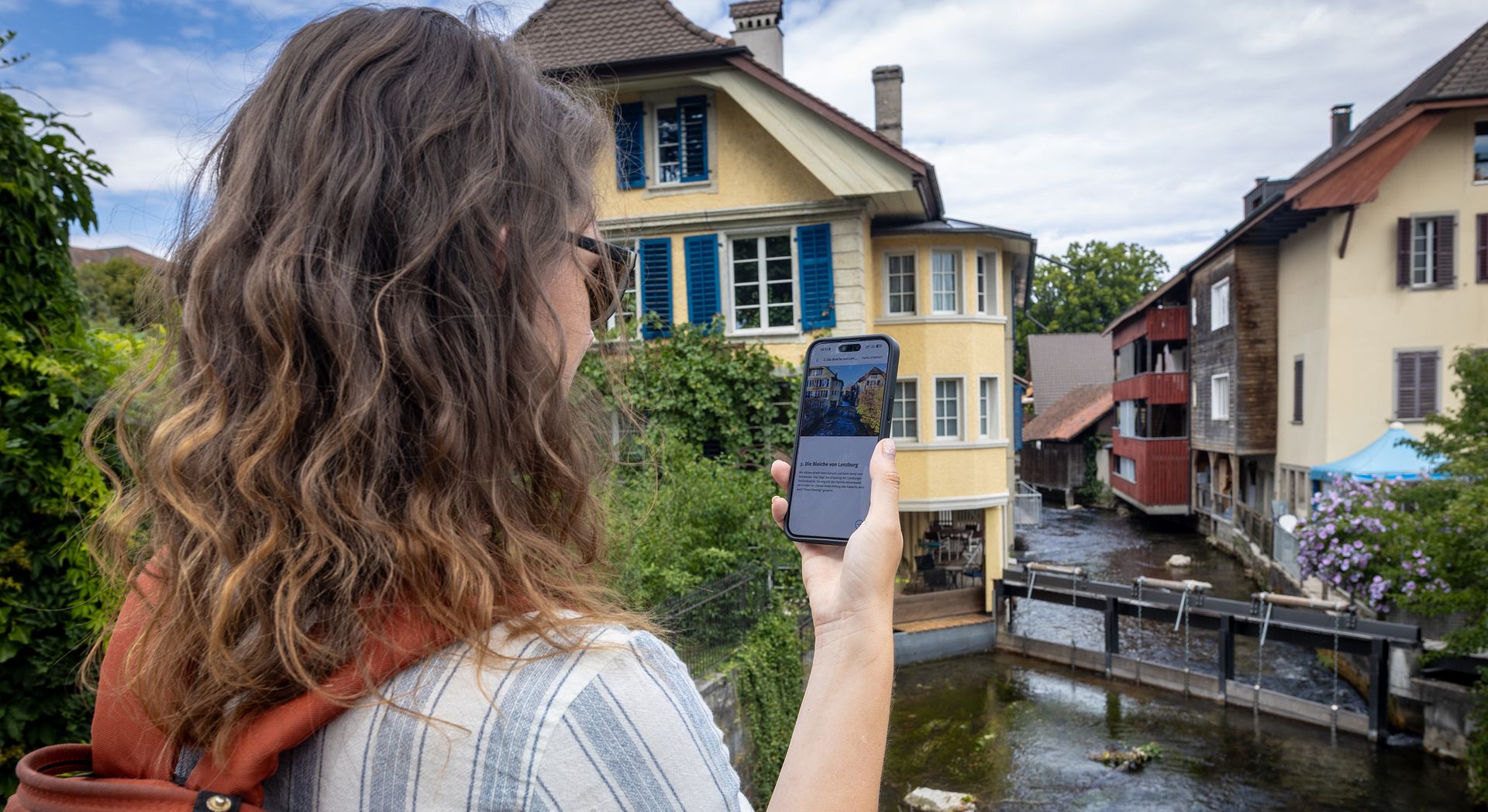 Eine Frau steht mit einem Handy in der Hand an einem Fluss.