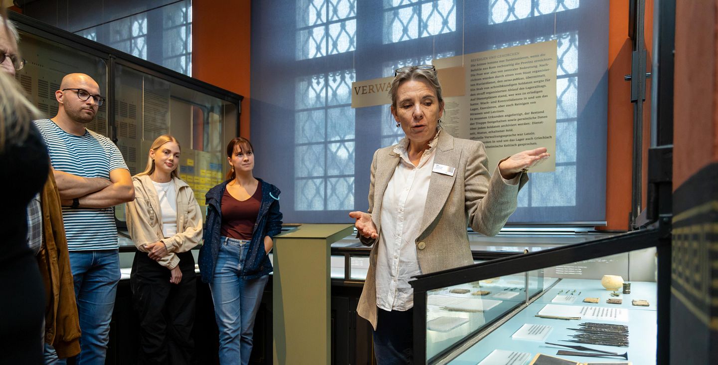 Eine Frau erklärt mehreren Besuchenden unterschiedliche Objekte in einer Vitrine im Vindonissa-Museum