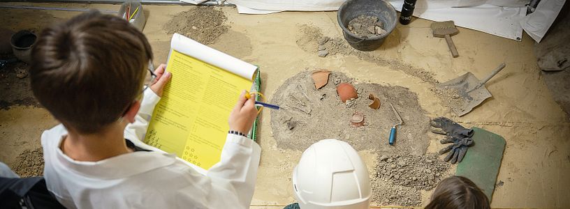 Kinder als Forscherinnen und Forscher verkleidet begutachten die Ausstellung und lösen Rätsel (Aufnahme von Oben)