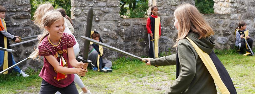 Workshop "Feste Burg Schloss Hallwyl" Kinder haben zusammen spass im Schwertkampf mit Zinnen im Hintergrund