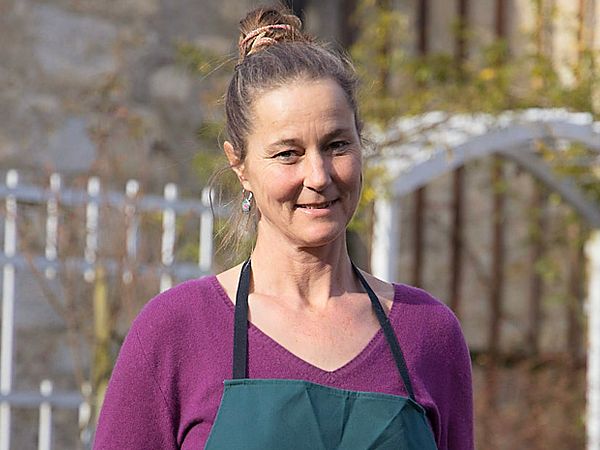 Eine Frau mit Gärtnerkleidung steht in einem Garten.