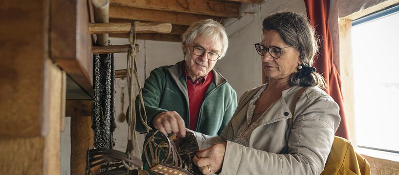 Ein Mann und eine Frau stehen in einer römischen Legionärsunterkunft. Sie betrachten römische Sandalen.