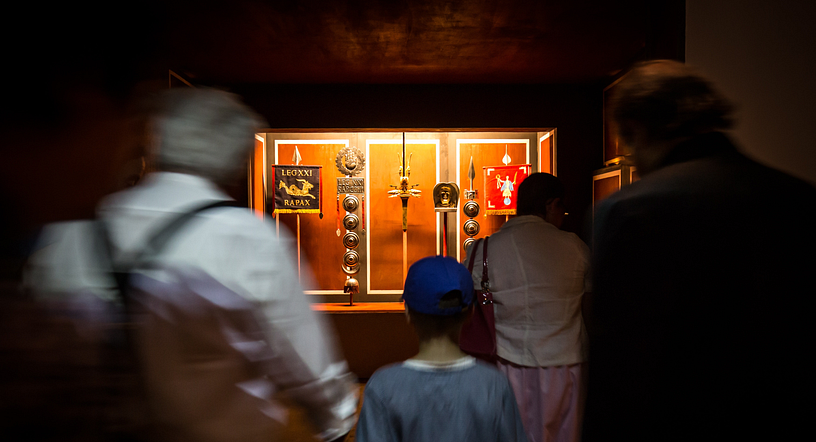 Ein mystisch erleuchteter Raum mit römischen Objekten, im Vordergrund mehrere Personen