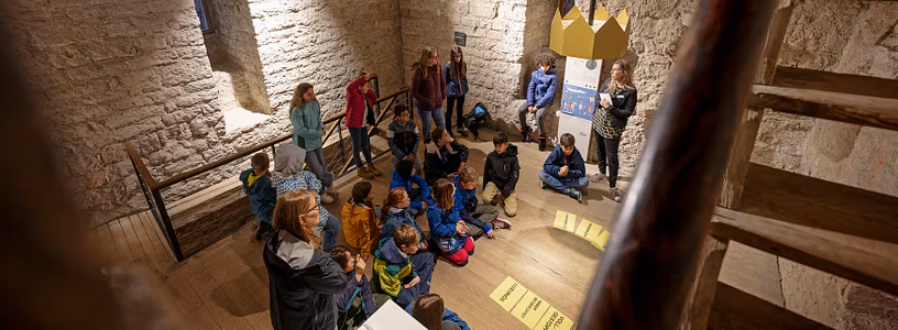 Eine Schulklasse sitzt im Kreis im Innern von Schloss Habsburg; am Boden liegen Blätter mit Texten.