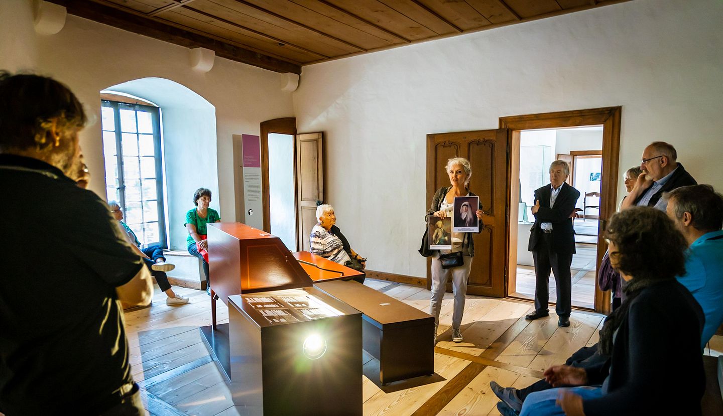 Eine Museumsführerin steht mit einer Gästegruppe in einem Museumsraum von Schloss Hallwyl.