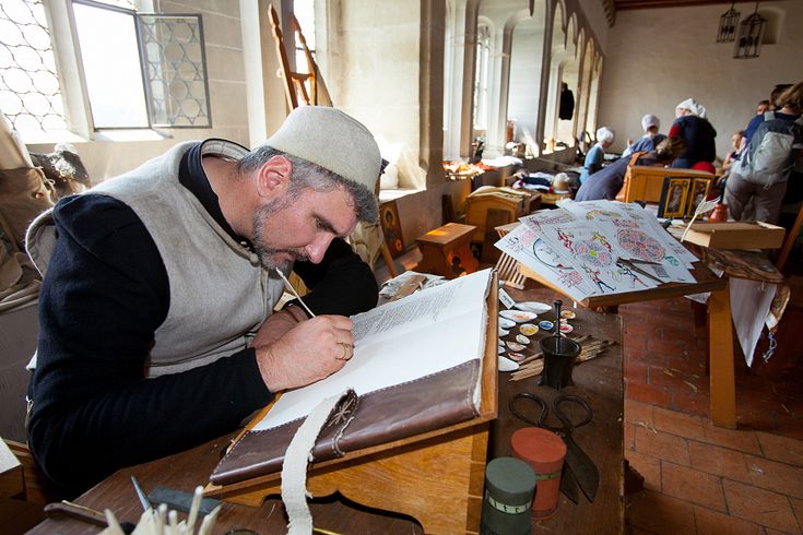 Ein mittelalterlich gekleideter Mann schreibt in einem Buch