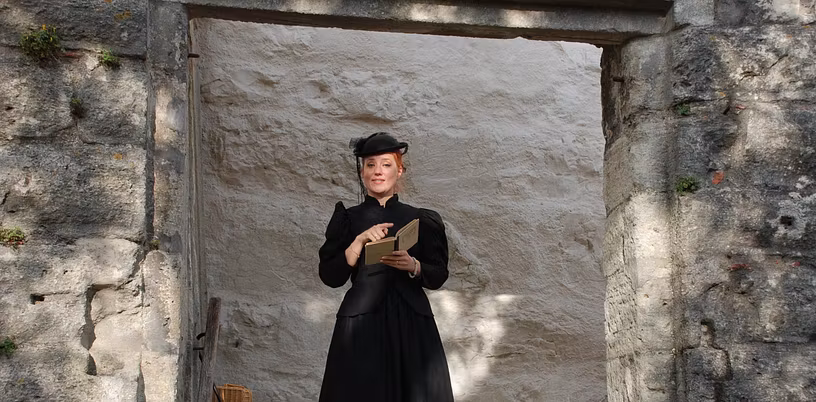 Eine als Gouvernante verkleidete Frau mit Buch auf Schloss Wildegg (blickt direkt in die Kamera)