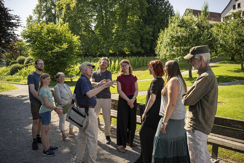 Besucherinnen und Besucher mit einem Museumsführer stehen im Park der Klostesrhalbinsel Wettingen