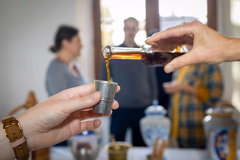 Hand, die eine Tinktur in ein Glas füllt. Im Hintergrund eine Besuchergruppe auf Schloss Hallwyl.