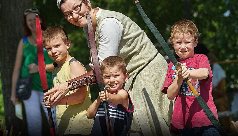 Drei Kinder mit Pfeilbogen. Sie blicken direkt in die Kamera.