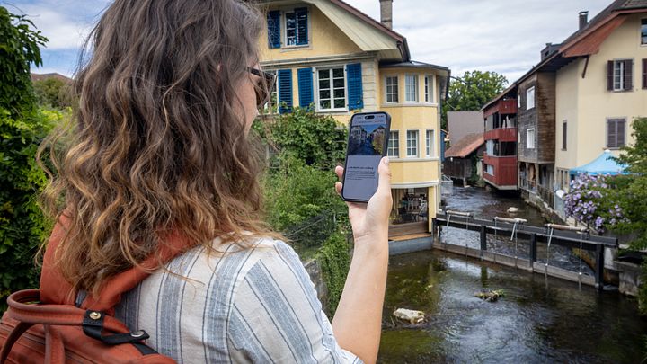 Eine Frau steht mit einem Handy in der Hand an einem Fluss.