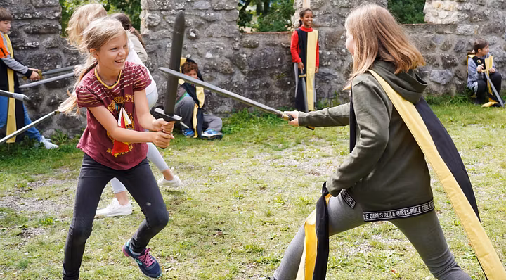 Workshop "Feste Burg Schloss Hallwyl" Kinder haben zusammen spass im Schwertkampf mit Zinnen im Hintergrund