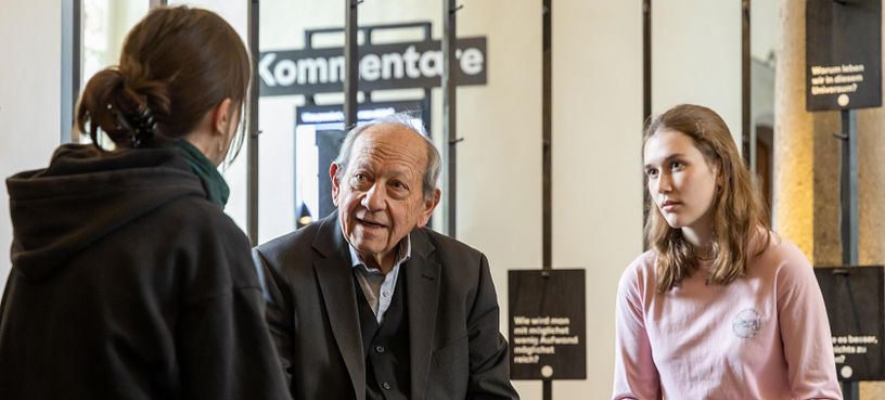 Ausstellungsraum im Parlatorium der Klosterhalbinsel Wettingen: Ein älterer Mann im Gespräch mit zwei Schülerinnen.
