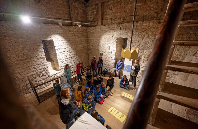 Eine Schulklasse sitzt im Kreis im Innern von Schloss Habsburg; am Boden liegen Blätter mit Texten.