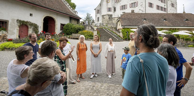 Eine Museumsführerin steht mit einer Gruppe aus Besucherinnen und Besuchern im Hof von Schloss Wildegg.