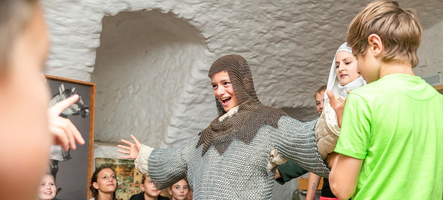 Gruppe von Kindern umringen einen Jungen, der ein Kettenhemd angezogen hat auf Schloss Lenzburg