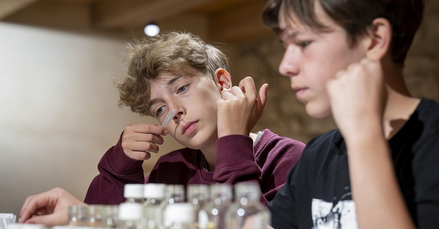 Ein junger Mann riecht an einem Riechstab, vor ihm steht eine Duftorgel mit verschiednenen Duftnoten