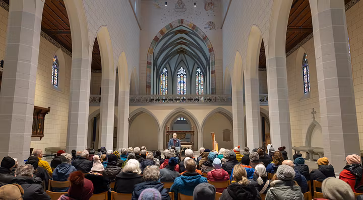 Innenraum Kloster Königsfeld mit vielen Gästen, die sitzen. Vorne spricht ein Mann an einem Podium.
