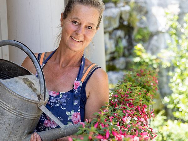 Eine Frau giesst Blumen mit einer Giesskanne im Garten von Schloss Wildegg.