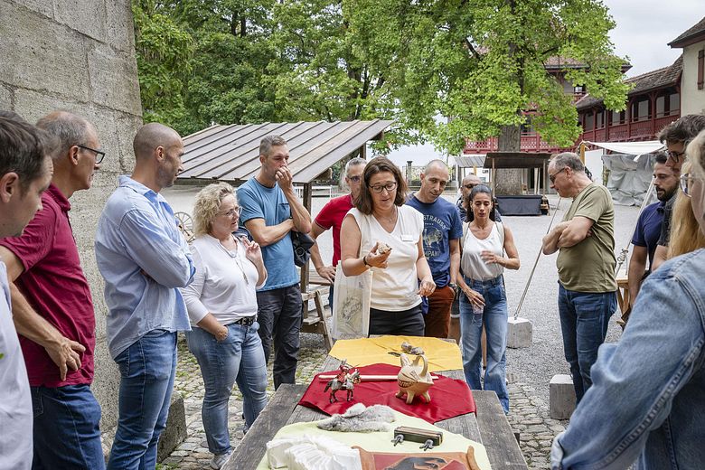 Eine Museumsführerin steht mit Besucherinnen und Besucher um einen grossen Tisch mit verschiedenen Objekten. Im Hintergrund der Hof von Schloss Lenzburg
