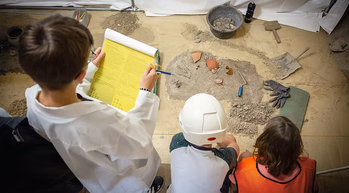 Kinder als Forscherinnen und Forscher verkleidet begutachten die Ausstellung und lösen Rätsel (Aufnahme von Oben)
