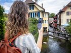 Eine Frau steht mit einem Handy in der Hand an einem Fluss.