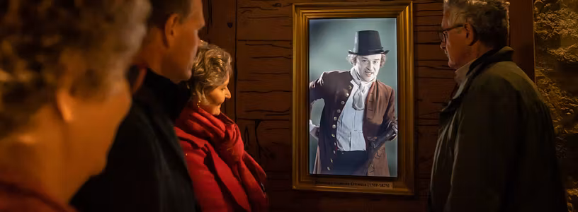 Besucherinnen und Besuche betrachten ein sprechendes Video-Porträt in der Ausstellung von Schloss Wildegg.