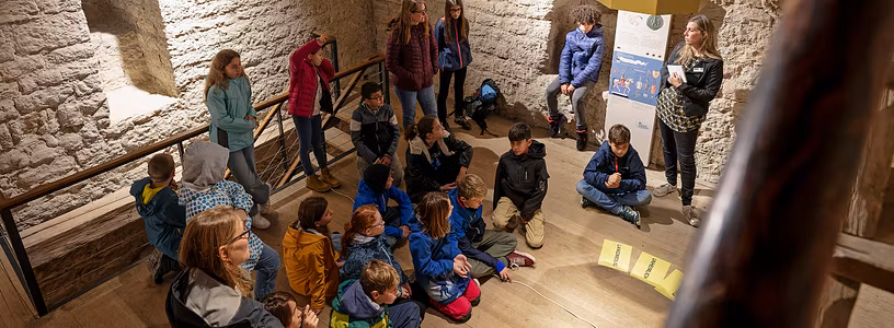 Eine Schulklasse sitzt im Kreis im Innern von Schloss Habsburg; am Boden liegen Blätter mit Texten.