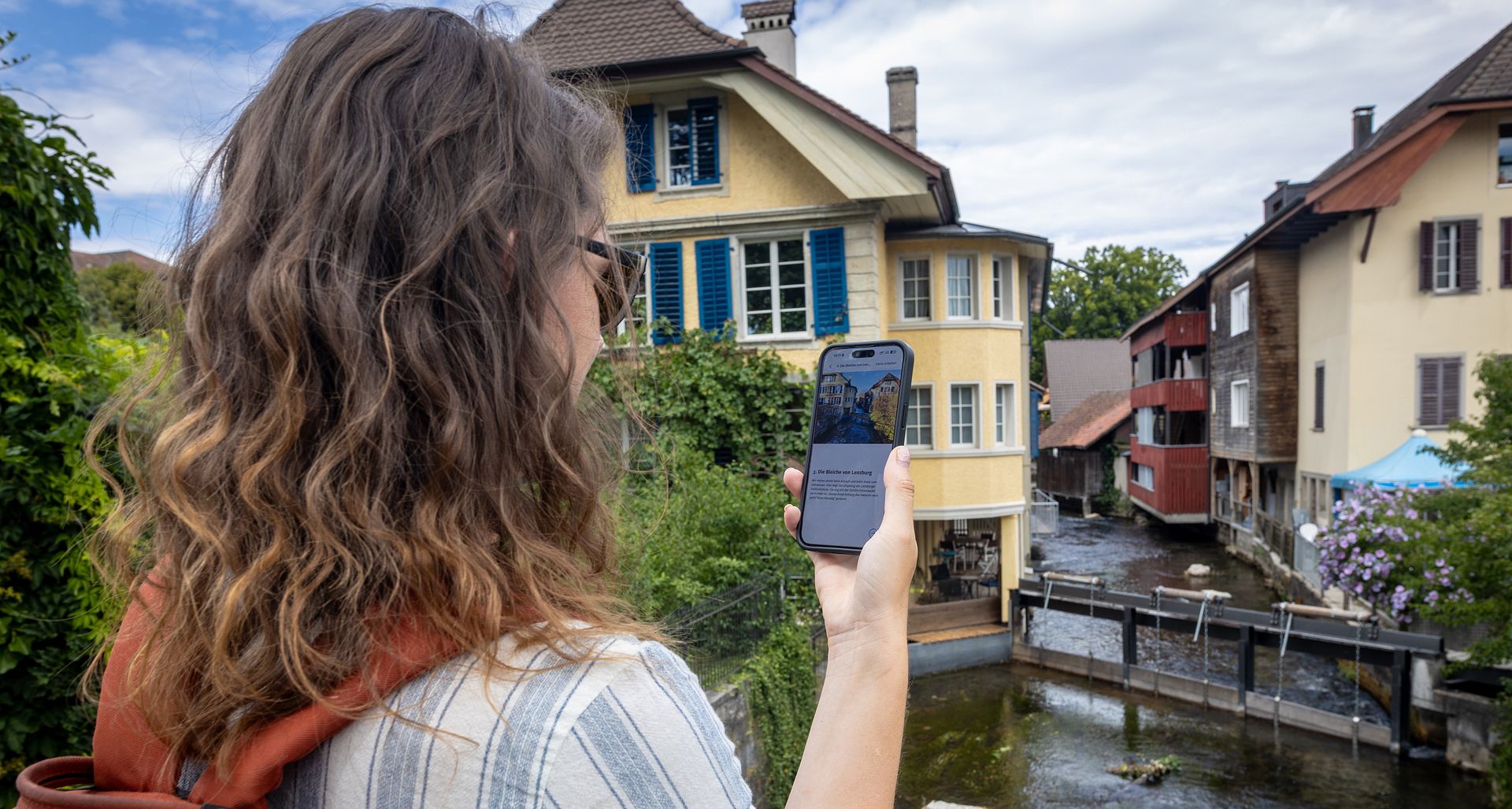 Eine Frau steht mit einem Handy in der Hand an einem Fluss.