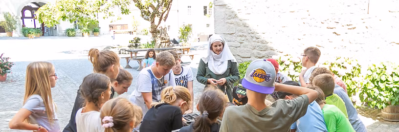 Eine Schulklasse steht versammelt um einen Brunnen während der Führung "Alltag im Mittelalter" auf Schloss Lenzburg.