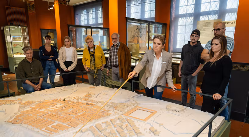 Eine Gästegruppe mit Museumsführerin. Die Gruppe steht um ein grosses Modell des Legionslagers Vindonissa.