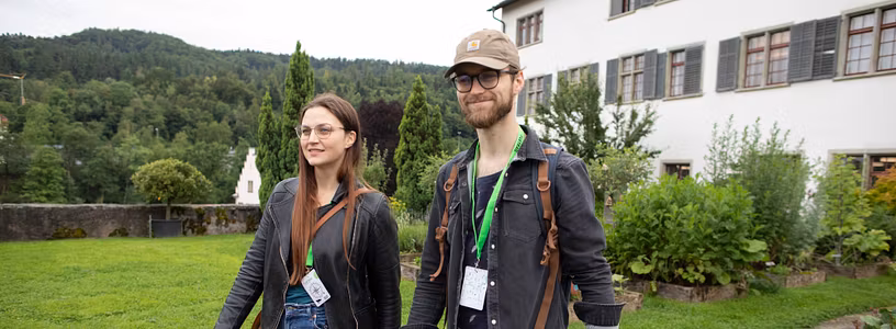 Eine Frau und ein Mann schreiten in Freizeitbekleidung durch den Garten der Klosterhalbinsel Wettingen (Foxtrail).