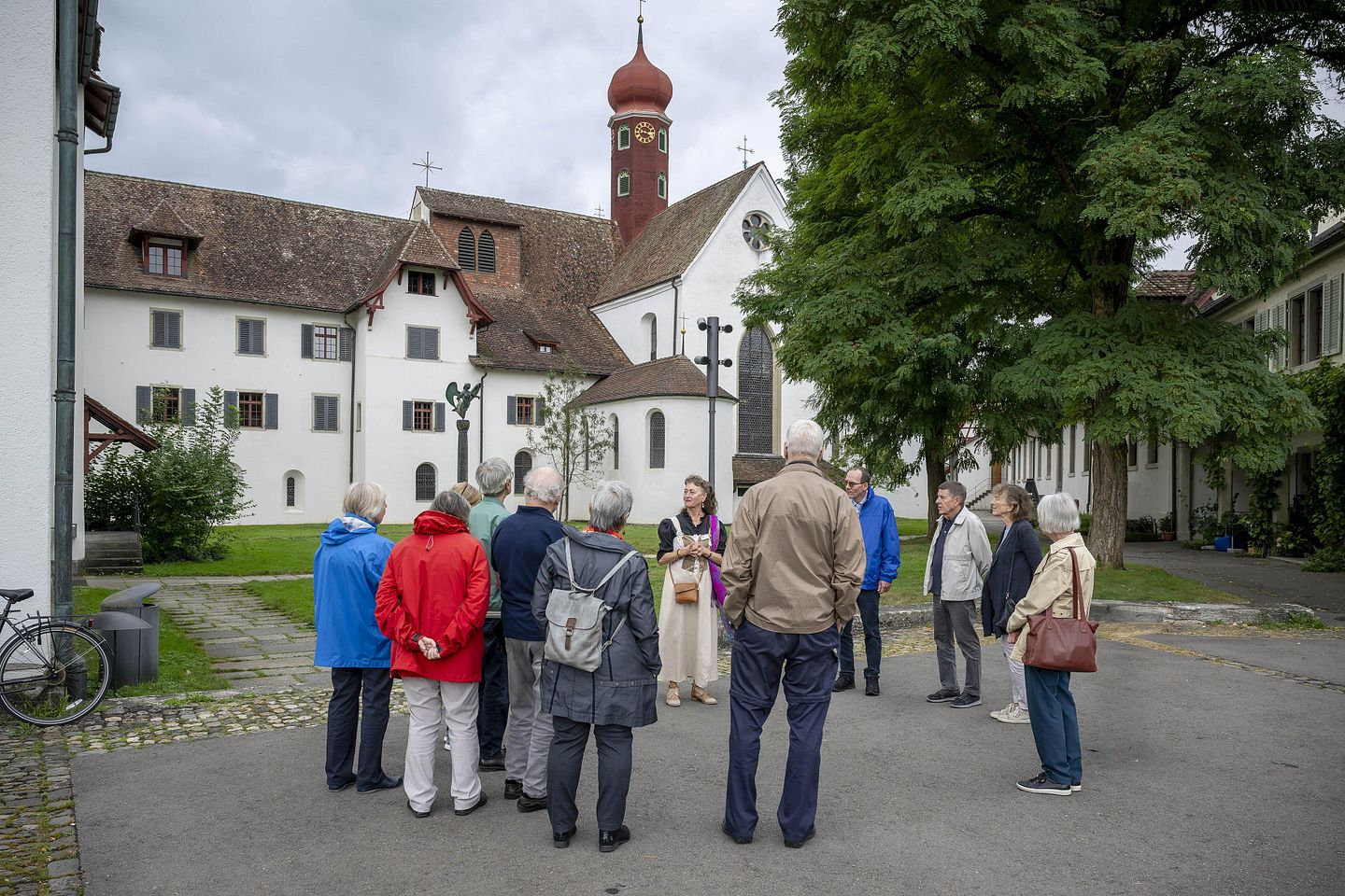 Eine Gruppe Besucherinnen und Besucher steht mit einer Museumsführerin vor dem Kloster Wettingen. Im Hintergrund die Klosterkirche.