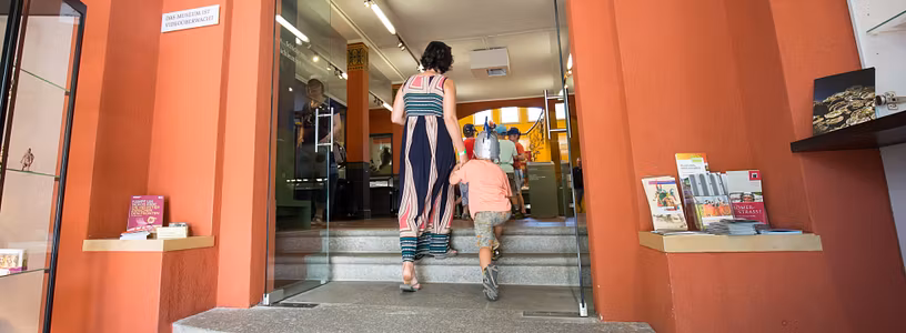 Besucher*innen betreten das Vindonissa Museum mit der grossen Orangen Eingangstüre