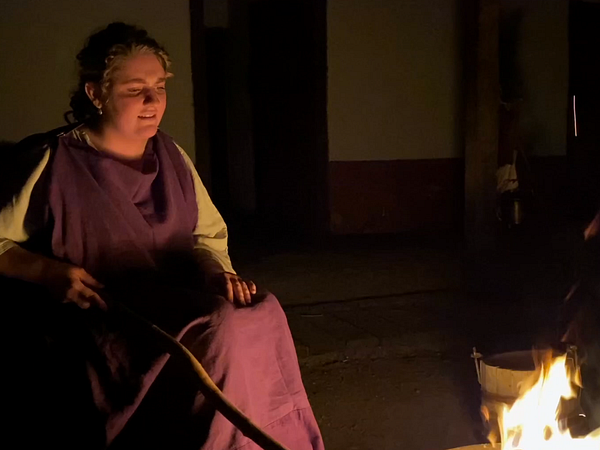 Eine als Römerin verkleidete Frau sitzt an einem Lagerfeuer in der Gasser der Mannschaftsunterkunft im Legionärspfad Vindonissa.