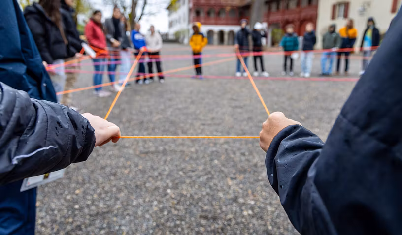 Schülerinnen und Schüler stehen in einem Kreis und sind mit einem Fadennetz verbunden