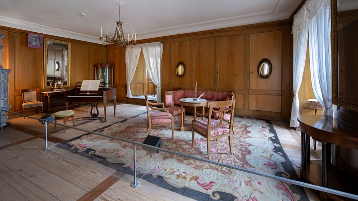 Ein Raum im Wohmuseum von Schloss Hallwyl mit Teppich, Klavier und weiteren Möbeln.