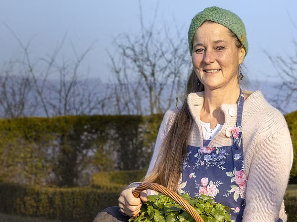Gärtnerin Tanya van der Laan kniend im Wildegger Schlossgarten. In den Händen hält sie einen geflochtenen Korb voller Minze.