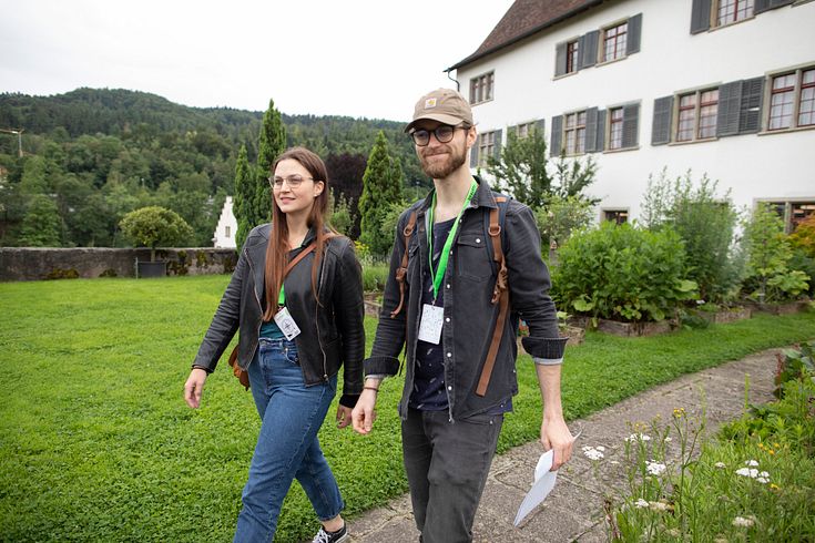 Eine Frau und ein Mann schreiten in Freizeitbekleidung durch den Garten der Klosterhalbinsel Wettingen (Foxtrail).