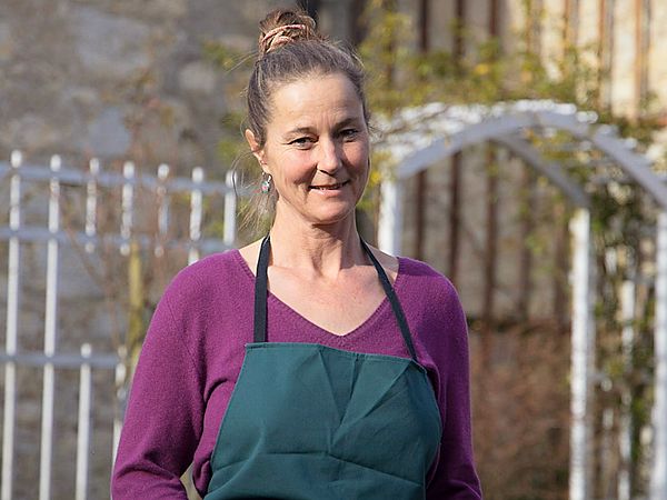 Eine Frau mit Gärtnerkleidung steht in einem Garten.