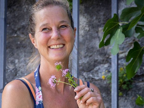 Porträt von Gärtnerin Tanya van der Laan. Sie befindet sich im Garten von Schloss Wildegg und hält gepflückte Blumen in der Hand. Im Hintergrund befindet sich eine Mauer mit einem Gitter.