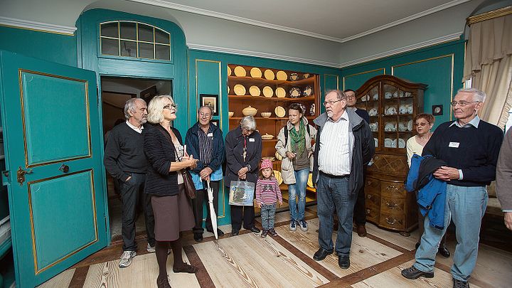 Besucher und Besucherinnen stehen in einem historischen Raum mit smaragdgrünen Wänden auf Schloss Wildegg und sind der Führerin zugewandt