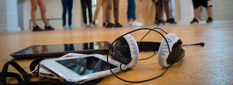 Audioguide-Gerät mit Kopfhörer, im Hintergrund in Unschärfe Schülerinnen und Schüler.