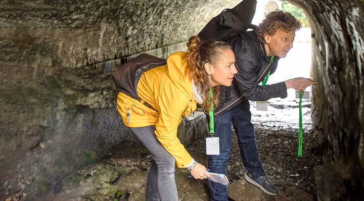 Eine Frau und ein Mann stehen in Freizeitkleidung in einer Höhle auf der Klosterhalbinsel Wettingen (Foxtrail). Sie blicken verwundert an die Wand rechts.